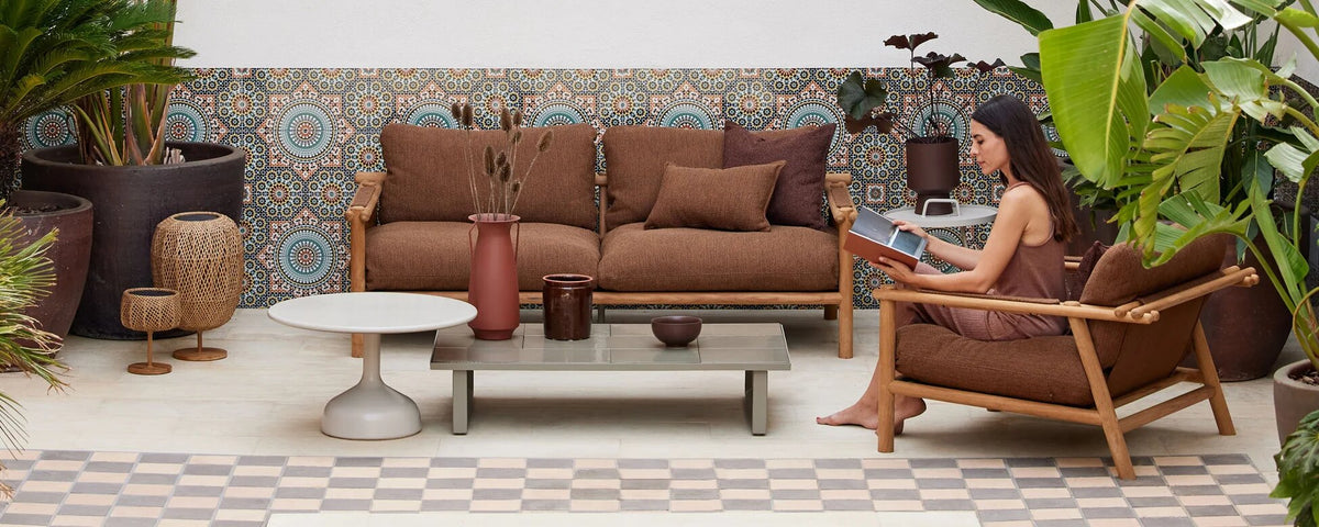 Cane-line Sticks teak sofa and lounge chair with a round Glaze coffee table on a tiled terrace