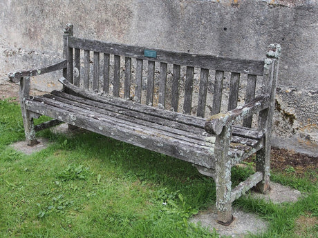 A weathered teak memorial bench with a brass plaque beneath an apple tree in a British garden