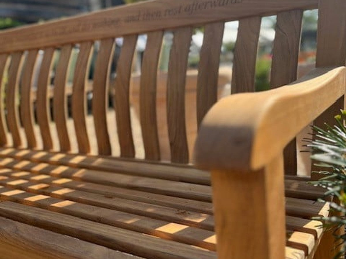 A weathered teak garden bench in a mature Surrey garden, showing the natural silver-grey patina of aged teak